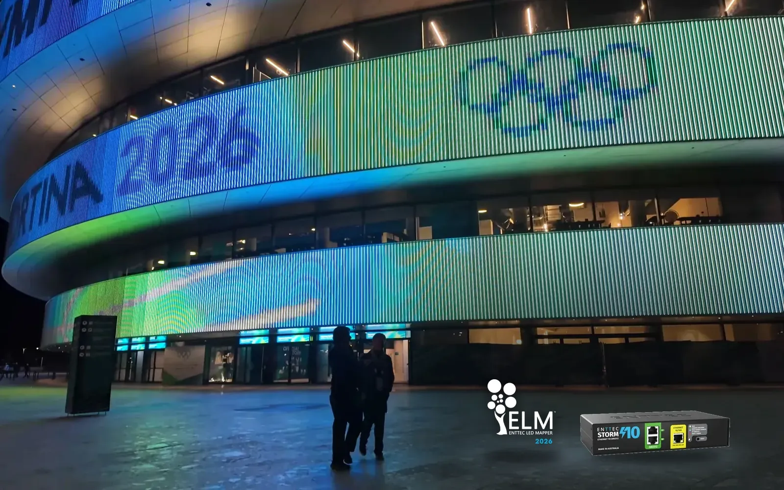 Arena Milano at night, its media facade lit with the Olympic rings and Milano Cortina 2026 branding