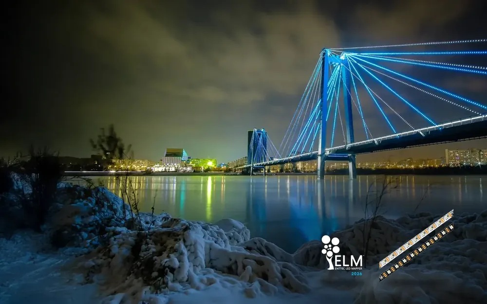 The Vinogradovsky footbridge at night from deck level, handrails glowing blue and orange with lit cables rising to the pylon