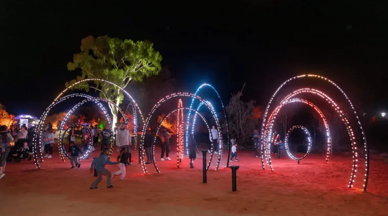 The completed hoops lit at night in red, blue and white, with visitors walking through the arcs