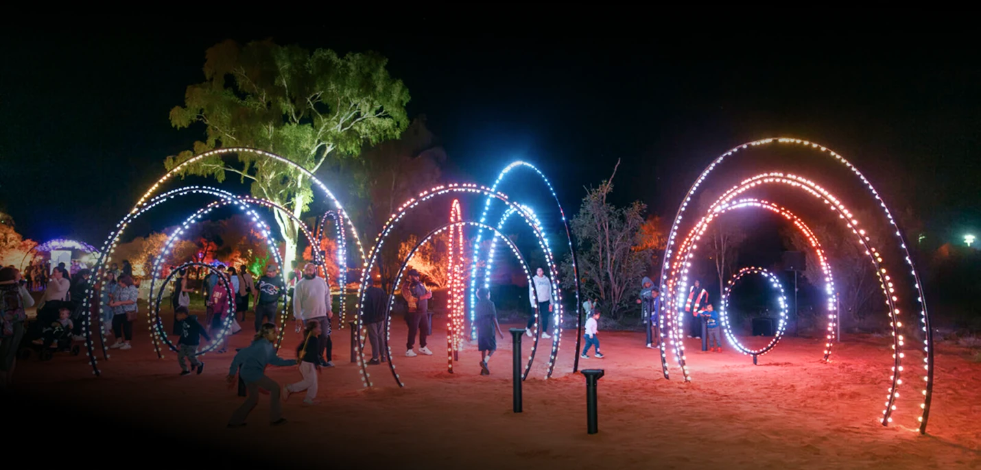 The Parrtjima hoop installation lit after dark, arcs of red, blue and white pixel dots with visitors walking beneath them