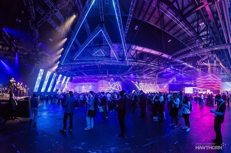 The exhibition hall in blue and purple, neon-lit triangles running the length of the roof above the crowd