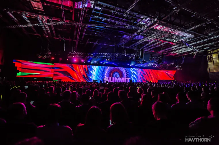 The main plenary, a wide LED screen in red and blue above a seated audience of thousands