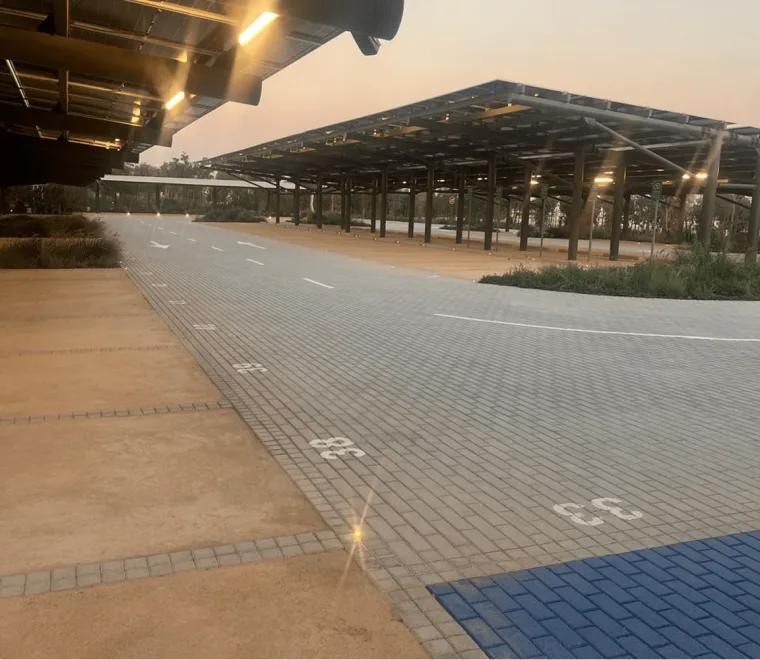 The car park under its solar canopy after sunset, downlights over the numbered bays and a clean run of paving