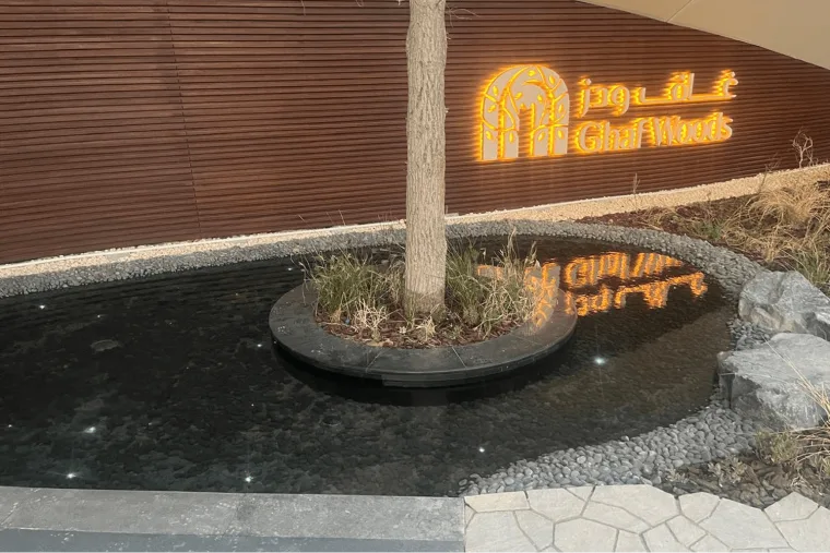 The same entrance wall from the driveway, a bare tree standing in a circular planter with dark water and gravel around it