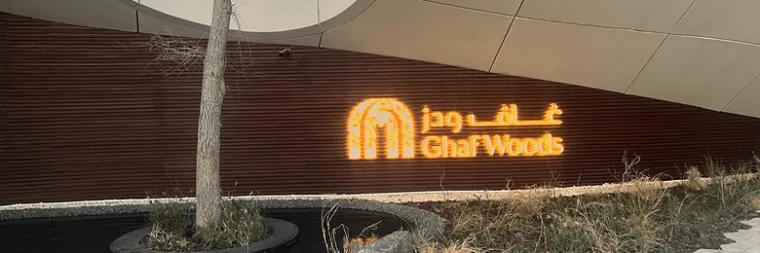 The lit entrance signage in Arabic and English on a slatted timber wall, tucked under the sweeping white soffit above
