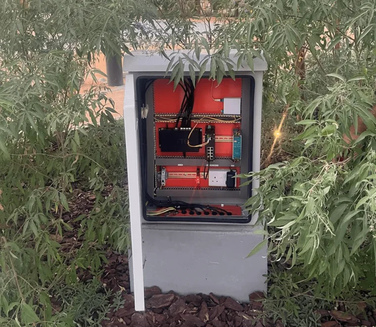 An open roadside control cabinet, its red backplate carrying a DIN mounted controller and terminal blocks with cabling dressed below