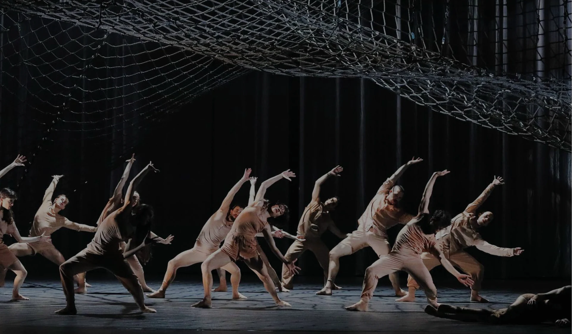 The net seen from the front with the company lunging forward in pale costumes, one dancer lying at the edge