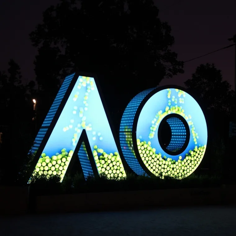 Blue sky and scattered tennis ball graphics running across the letters at night, green dots massed along the lower edge