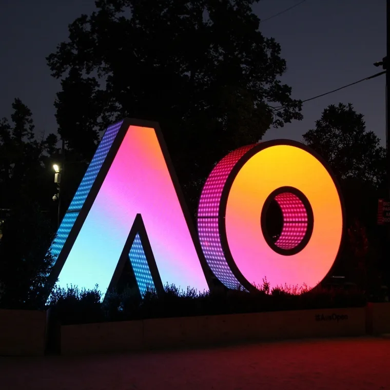 The letters washed in a pink to orange gradient at night, overhead power lines and dark trees behind