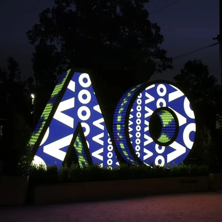 Deep blue with white chevrons and rings tiling the letters, the surrounding parkland in darkness
