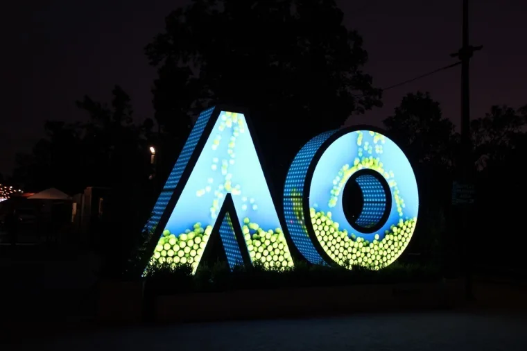 Wider night view from the left, sky and tennis ball artwork on the letters with path lights receding behind