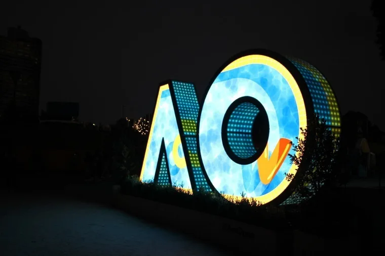 Cloud and sky artwork with a yellow tick across the letters, spectators walking past on the right at night