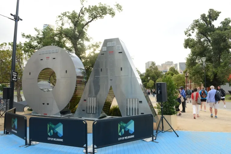 The unlit sculpture in daylight, bare grey letters on black plinths with City of Melbourne branding and passers-by