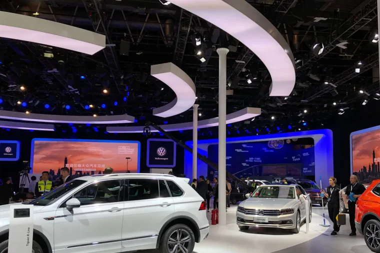 A white Tiguan and a white Passat under curved white ceiling ribbons, blue-lit walls and screens behind them