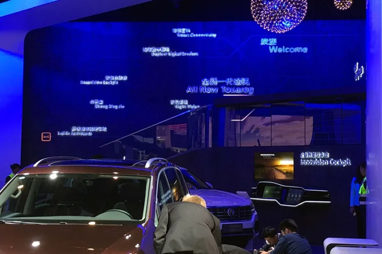 Blue-lit feature wall carrying glowing Chinese and English callouts including All New Touareg, a brown SUV parked in front