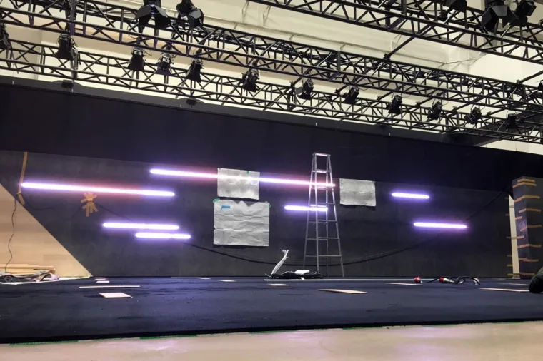 Build stage of the dark wall, pink and white pixel strips already lit, a step ladder alongside and moving lights on the truss above