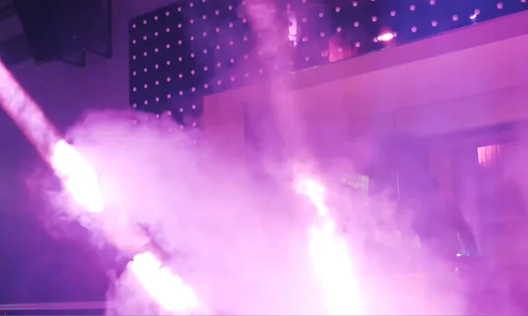Two beams of light cutting through thick pink haze over the dance floor, the dot wall glowing behind