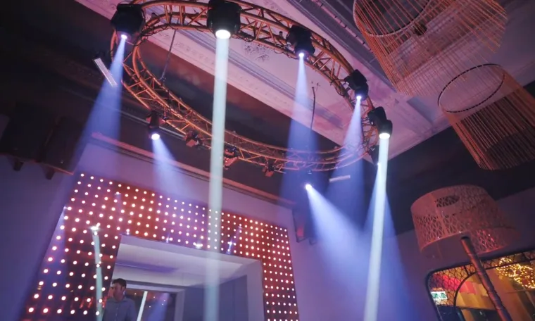 Moving heads on the circular truss firing white beams down through haze, the dot wall lit behind the booth