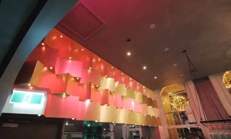The bar wall from further along, panels burning red and gold under the downlights with a green exit sign at the end