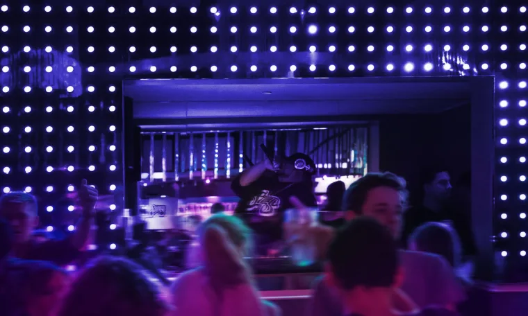 Clubbers on the dance floor seen through the dot wall, the grid lit blue and white above the crowd
