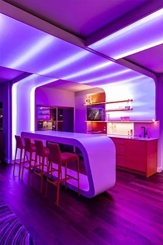 The bar lit deep purple and magenta, beams fanning across the ceiling above the curved white counter
