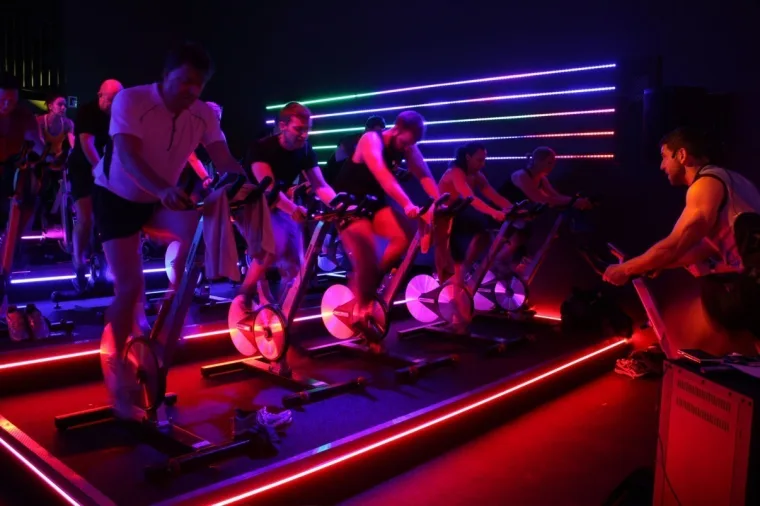 Riders side on with the strips running blue, pink and green, the floor line burning red beneath the bikes