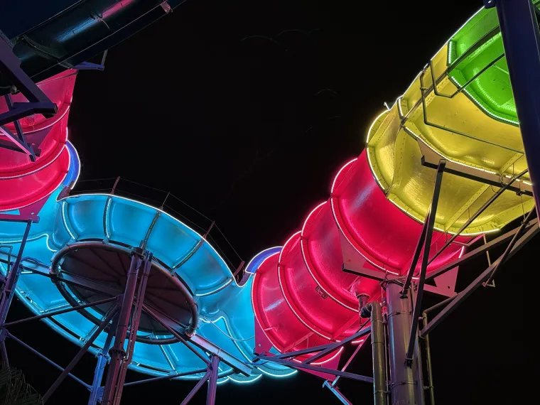 Two flumes looping side by side, one washed cyan, the other magenta and yellow green, against a black sky