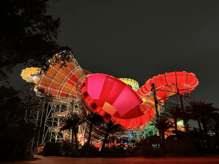 Wide night view of the tower complex, orange and red funnel bowls rising over palms with a green glow behind