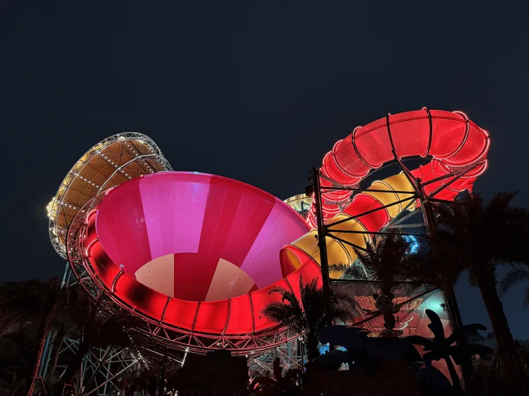 Closer on two funnel bowls, one open cone lit pink, the other deep red, lattice steelwork rising behind