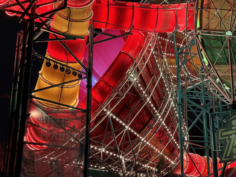 Red and orange bowls seen from below, warm string lights strung across the steel truss beneath them