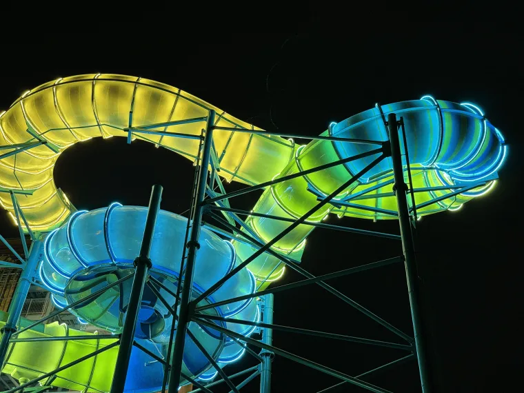 Yellow and cyan tubes looping into a figure of eight, thin steel masts crossing the black sky