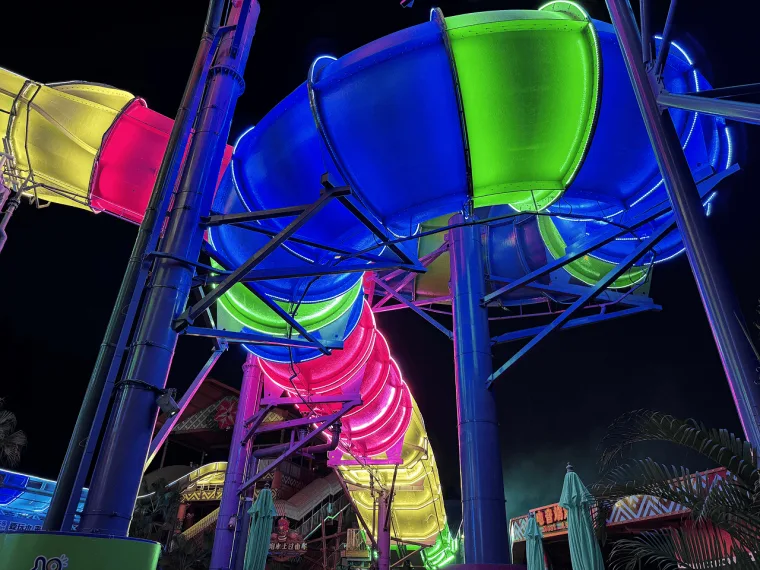 Blue and green tubes with pink and yellow sections below, seen from the ground between purple support poles