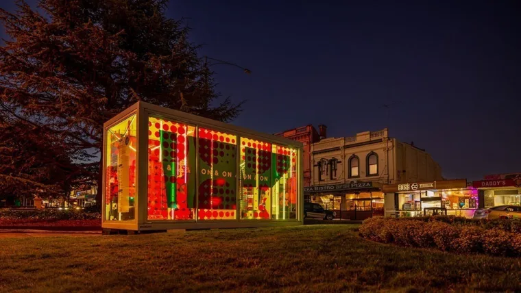 The Boom Box lit red and green after sunset on the Sturt Street median, shopfronts and a bare tree behind it