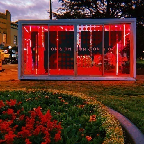 The Boom Box glowing red at dusk behind a bed of red flowers, ON & ON lettering repeated across the glass