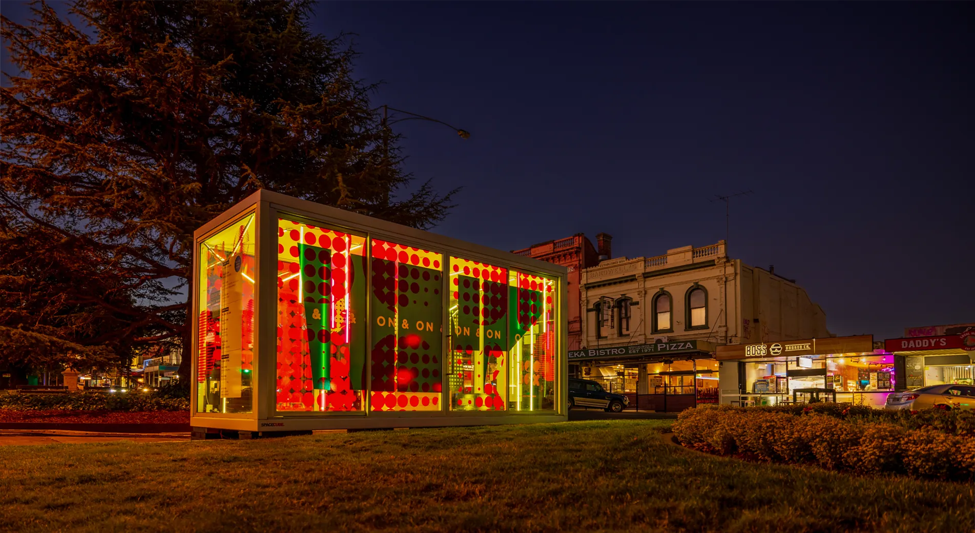 The Boom Box lit red and green at dusk on the Sturt Street median, ON & ON lettering across its glass panels and Ballarat shopfronts behind