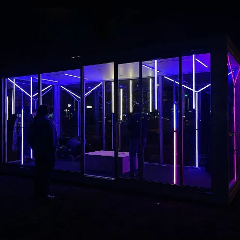 The Boom Box after dark from the front, blue and violet bars picking out the frame, two figures silhouetted against the glass