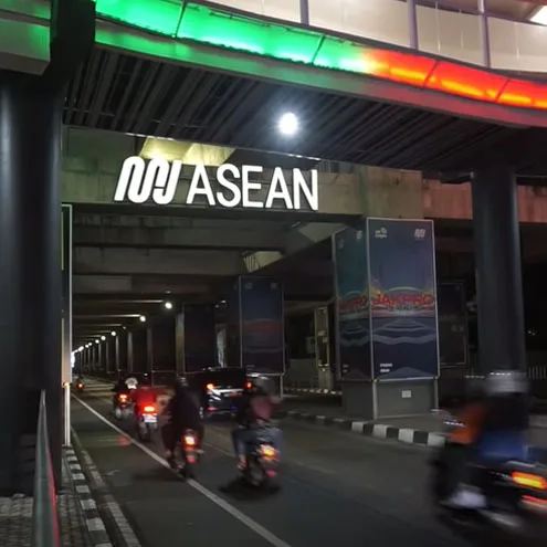 Traffic passing beneath the bridge under the illuminated ASEAN station sign, the canopy above lit green and red