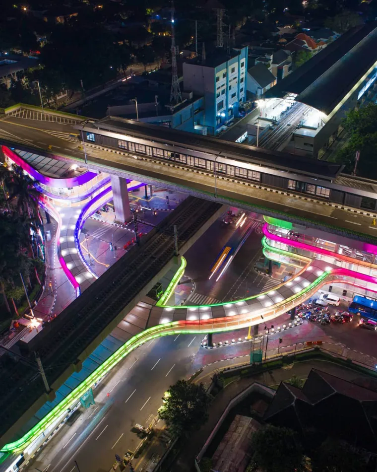 Aerial from higher up, long exposure light trails streaking the roads around the colour-lit bridge structure