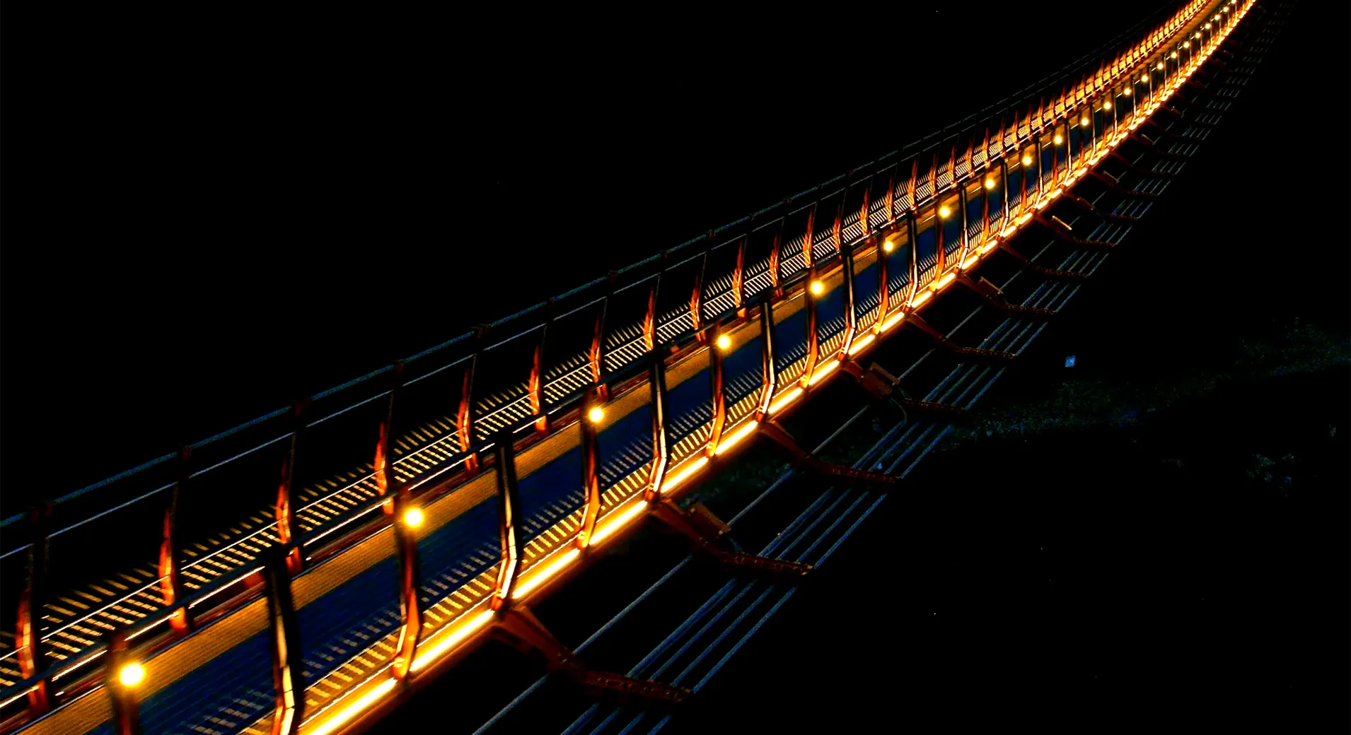 Daewangam Park footbridge after dark, amber pixel bars ranked along the handrail and blue light washing the deck as it curves away