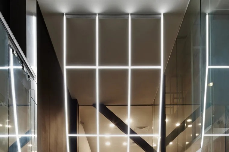 Close under the entrance element, the glowing grid folding overhead with ceiling downlights showing through behind it