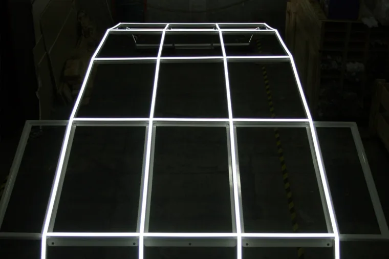 The custom LED frame lit and laid flat on a workshop floor before install, its grid of lines glowing white against the dark