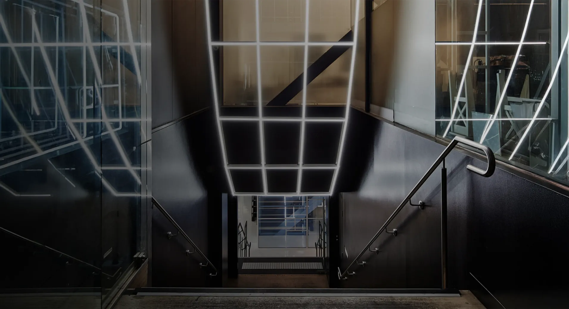Dust Redux's entrance element after dark, a cage of glowing white lines wrapping the stairwell with mirrored glass on both sides