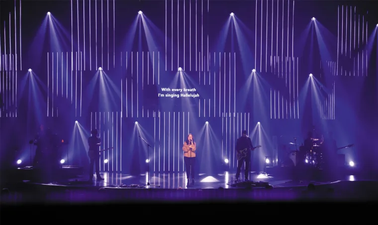 Violet wash across the stage with a single singer at centre, vertical strips and pools of downlight on the empty floor