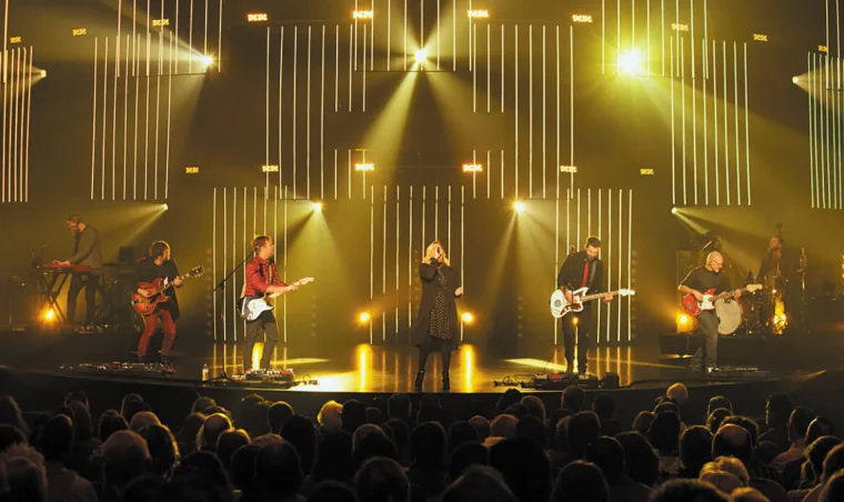 Warm gold wash with the vertical strips glowing amber, five musicians spread across the front of the stage