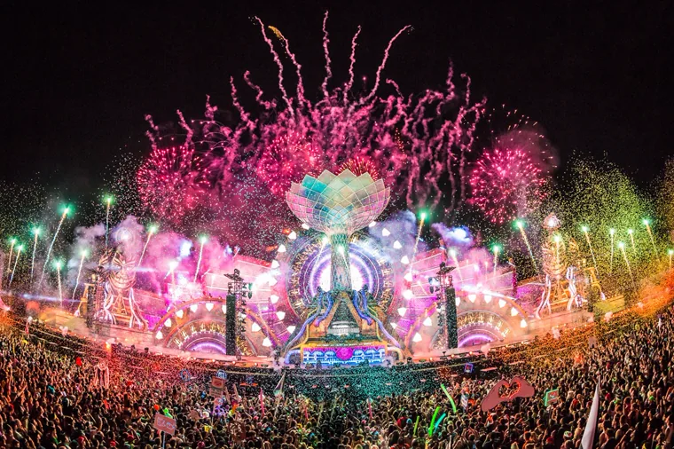 The main stage seen from across the crowd, magenta fireworks bursting above the pixel mapped canopy with the festival grounds lit behind