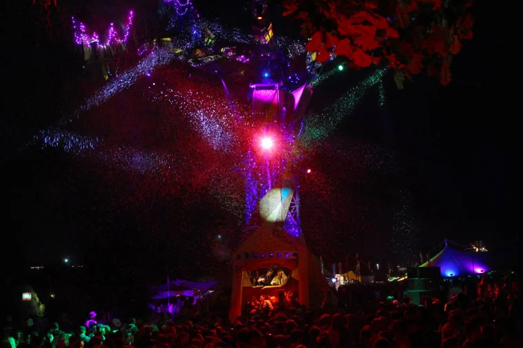 The tree seen from across the packed field, a pink beam and a spray of white light fanning out from its trunk