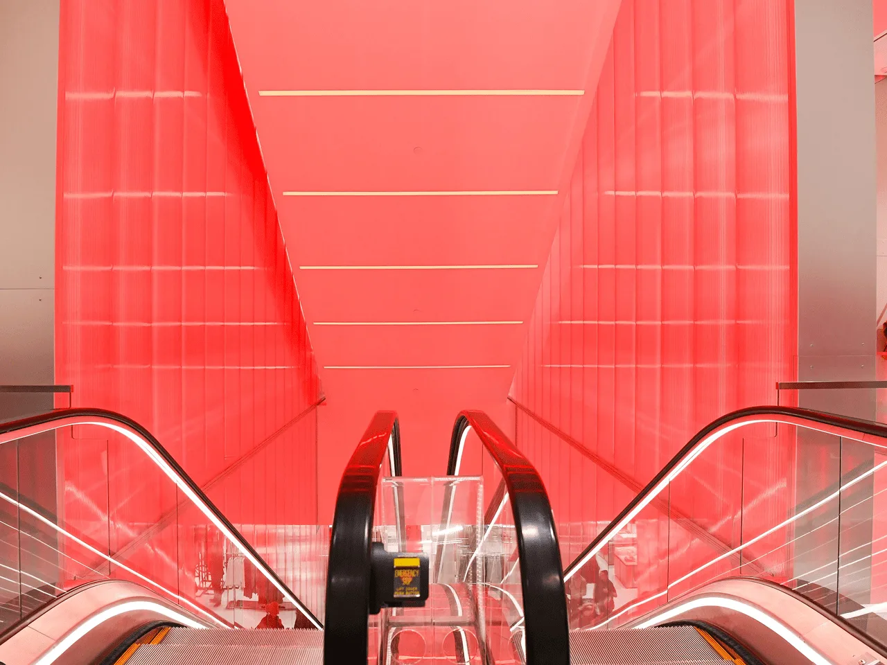 Looking straight up the escalator, red panels converging overhead where the walls meet the ceiling