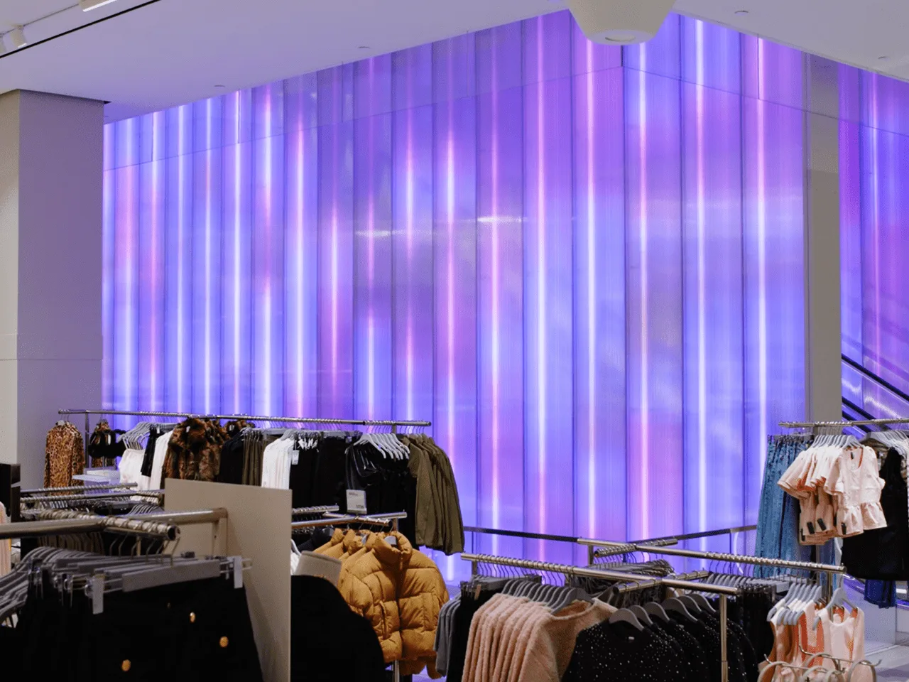 Clothing rails on the shop floor with the ribbed wall lit blue and violet behind them