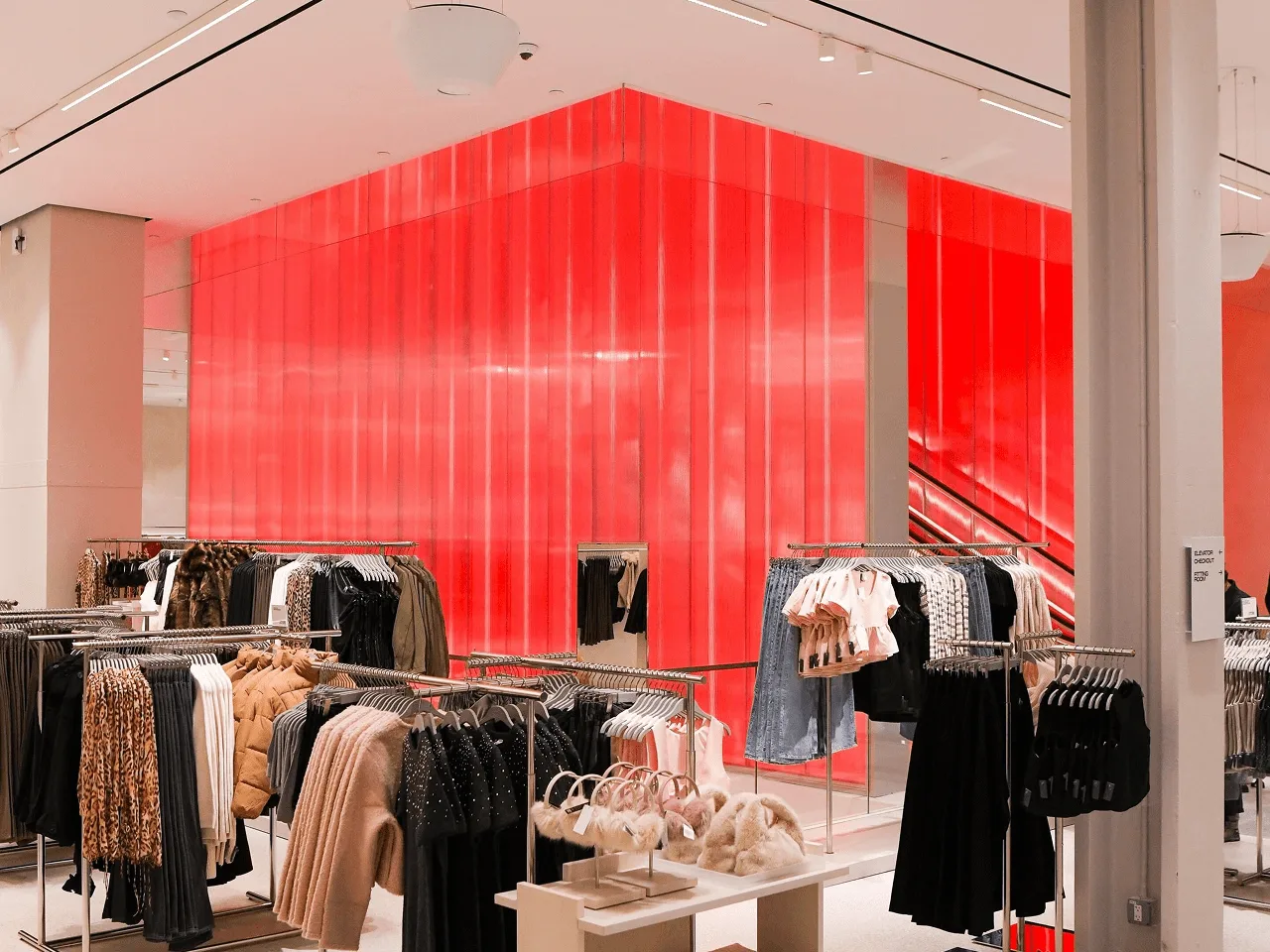 Rails of coats and knitwear in front of the same wall washed coral and red