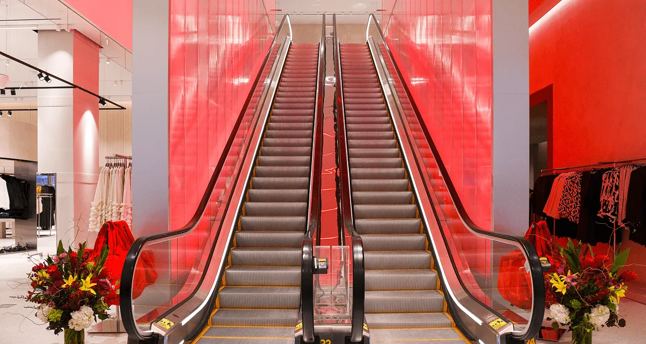 Both escalators head-on on opening day, flower arrangements at either side and the red lit wall filling the gap between them